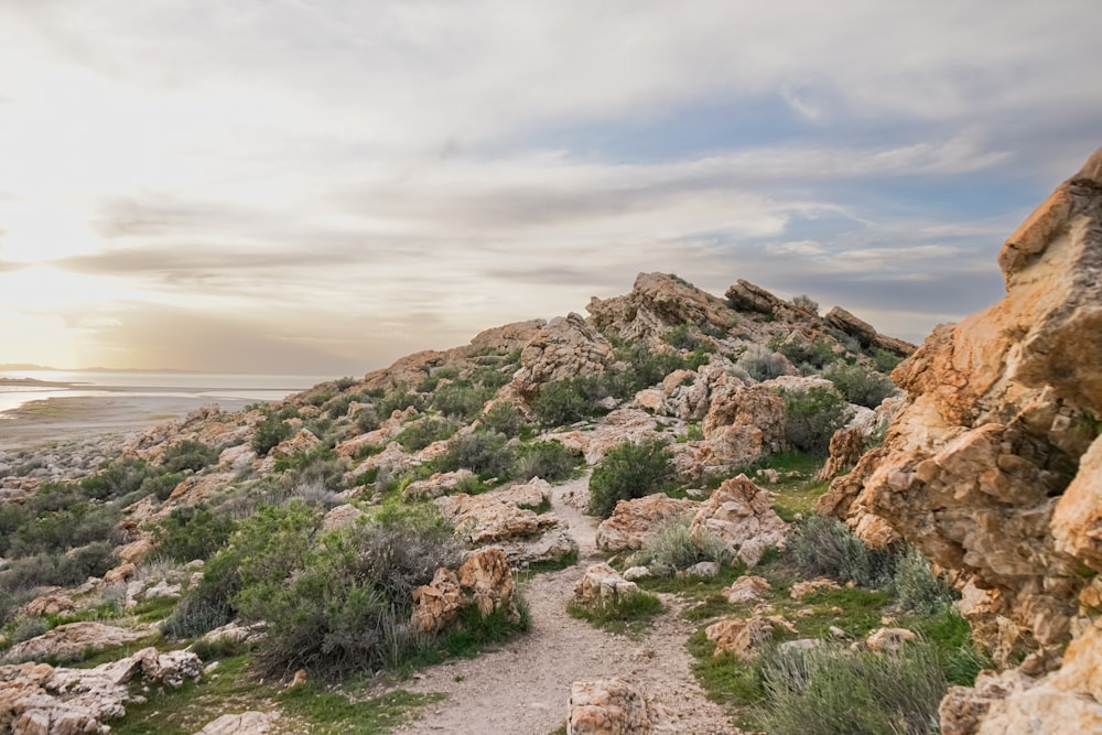 a dirt path going up a rocky hill next to a body of water