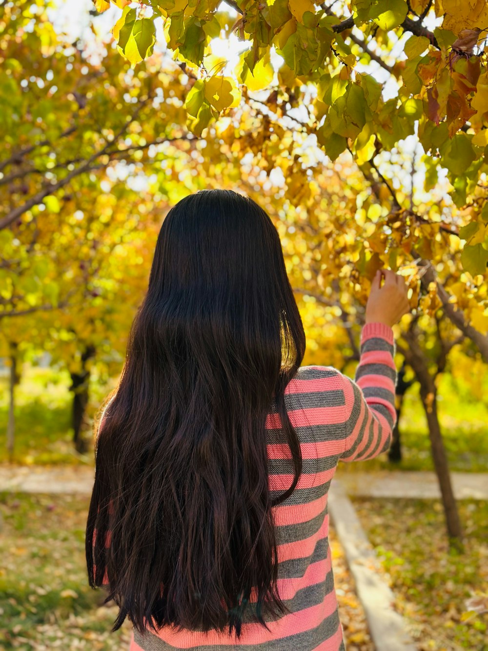 a woman standing in front of a tree with lots of leaves