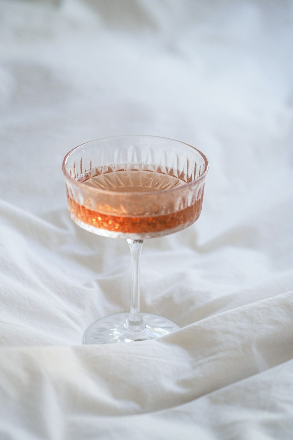a glass filled with a drink sitting on top of a bed