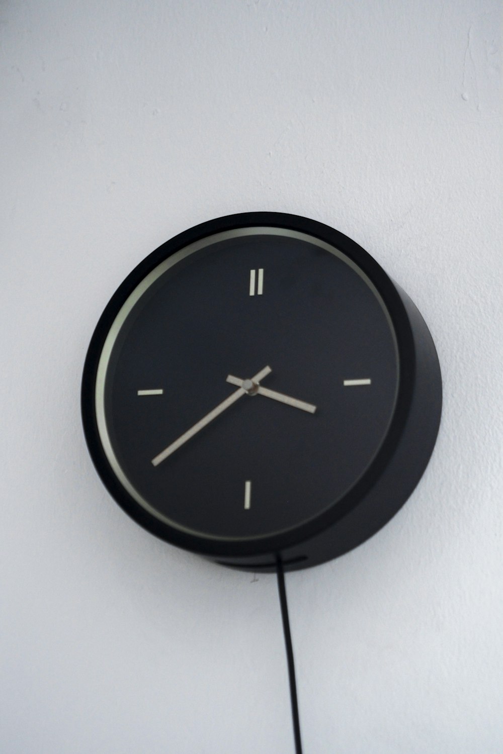 a black clock hanging on a white wall