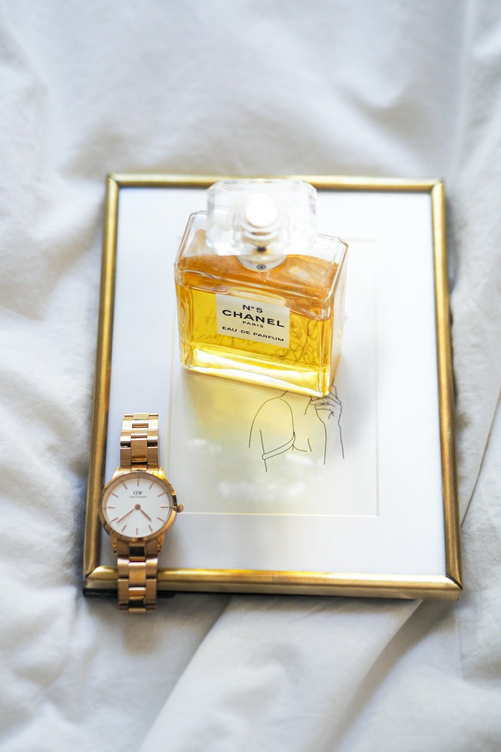 a watch and a bottle of perfume on a bed
