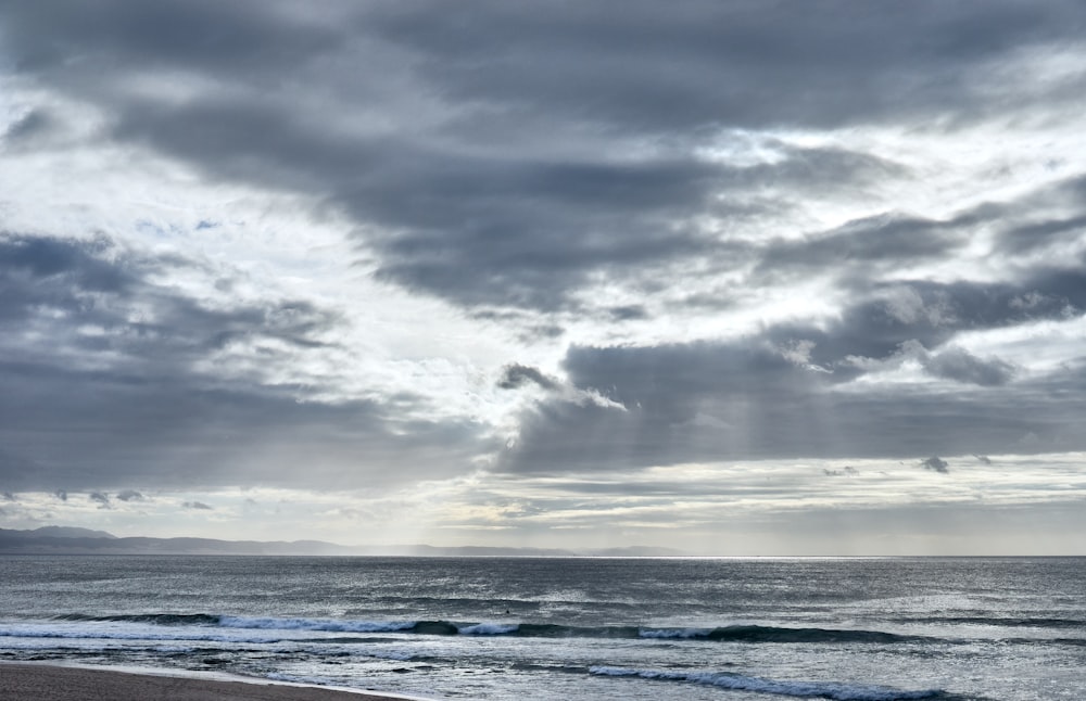 a cloudy sky over the ocean with a beach in the foreground