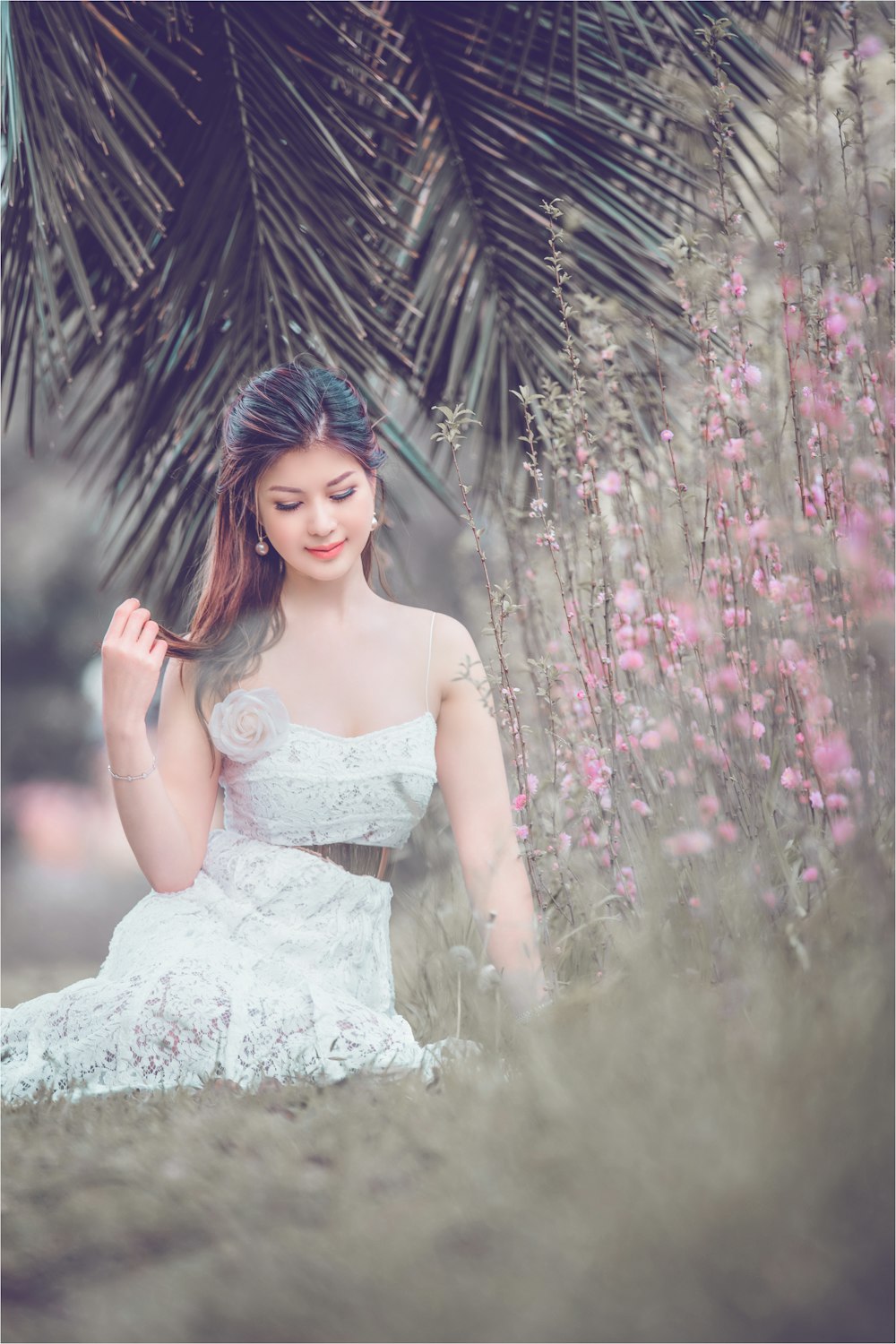 a woman in a white dress sitting under a palm tree