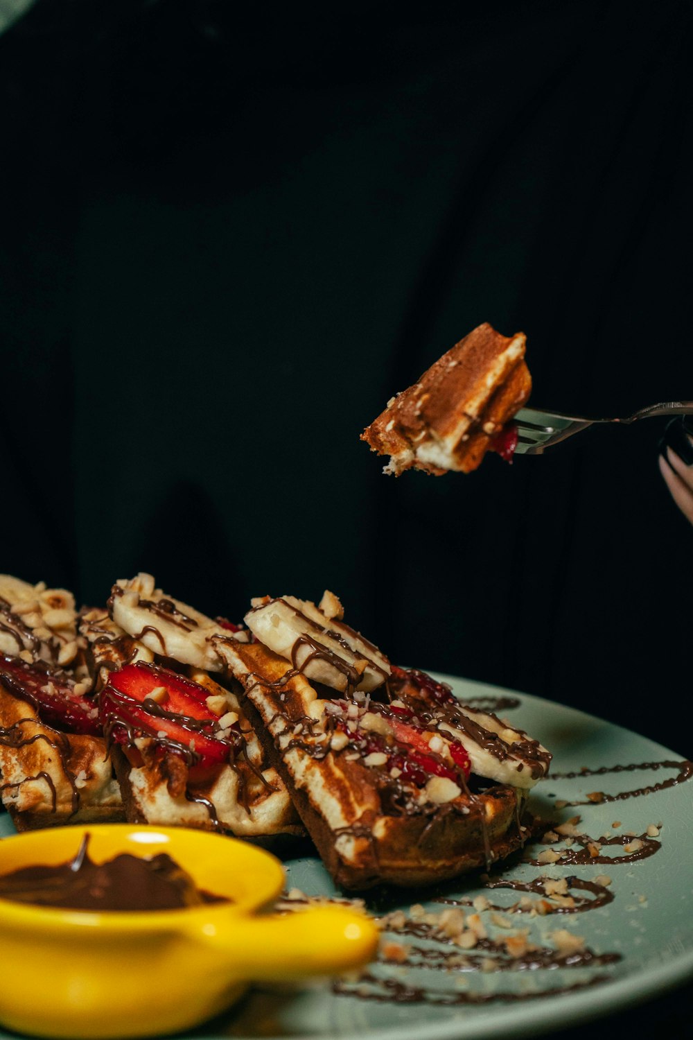 a person eating waffles with chocolate sauce and strawberries