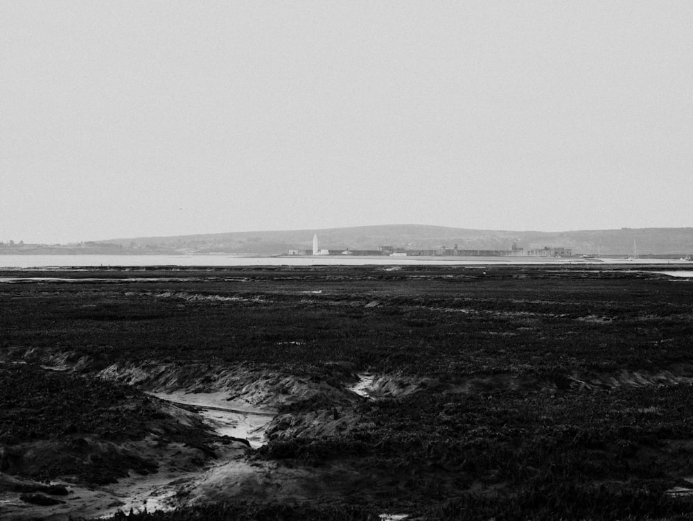 a black and white photo of a field with a lighthouse in the distance