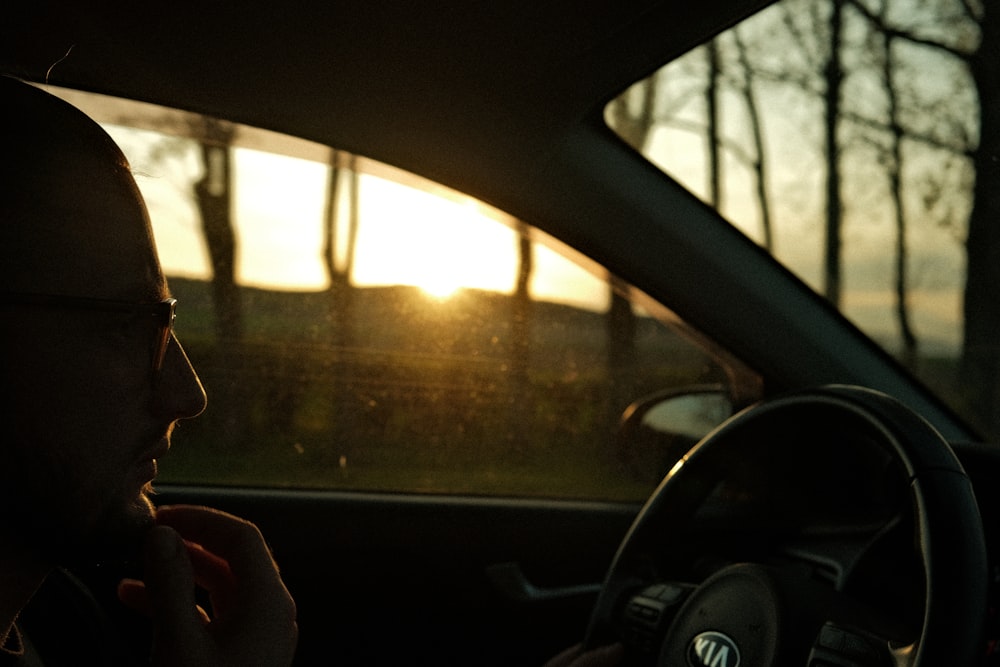 a man driving a car with the sun setting in the background