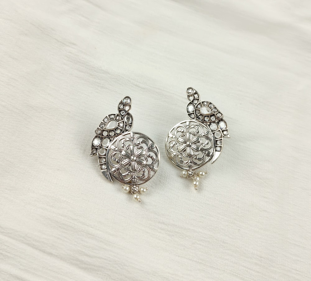 a pair of silver colored earrings on a white background