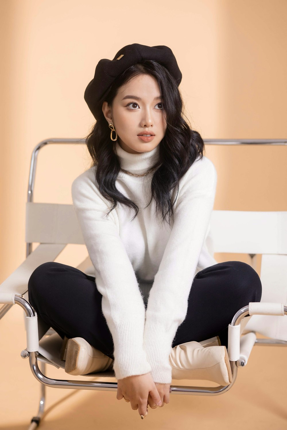 a woman sitting on a chair wearing a white sweater and black pants