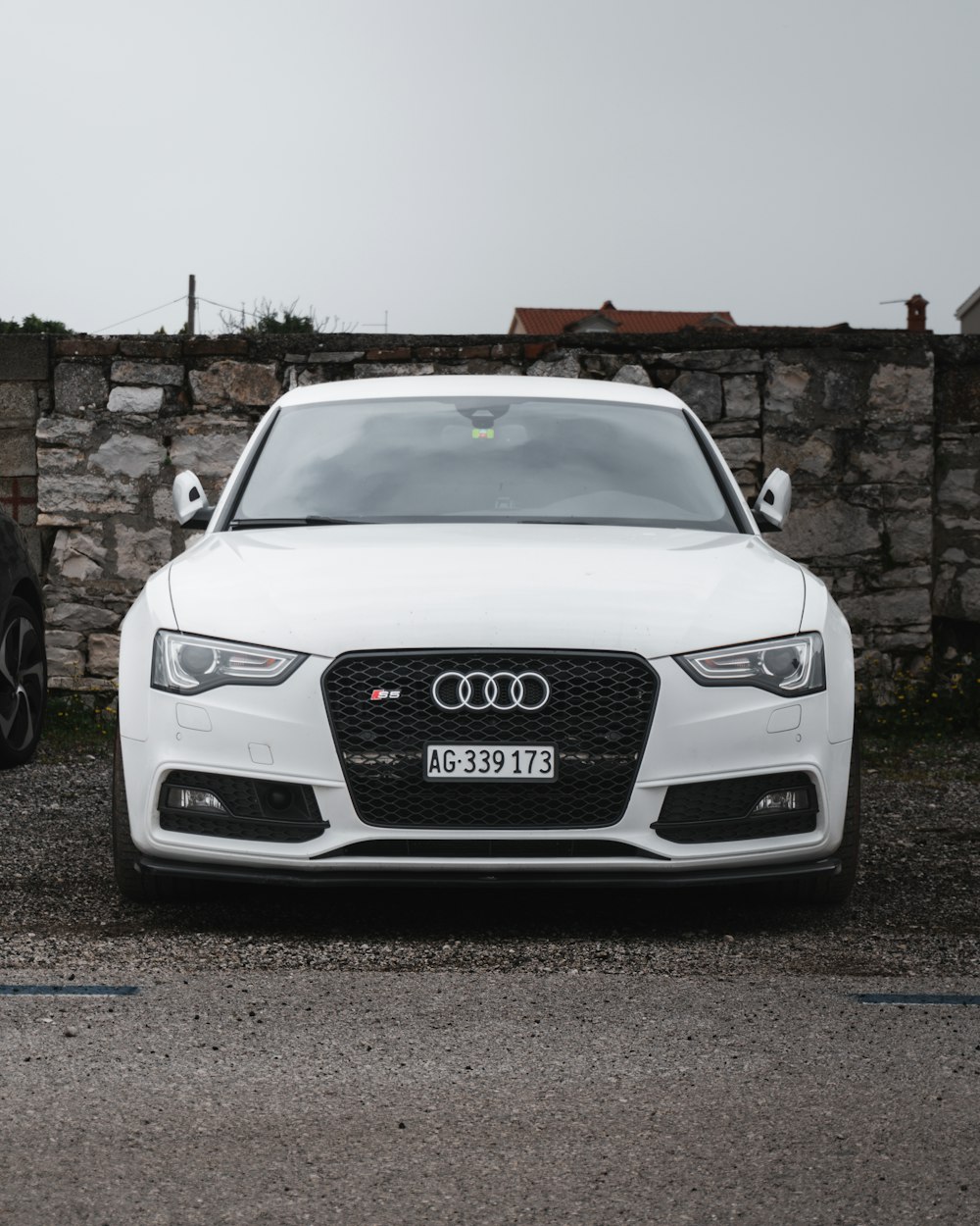 a white car parked in front of a stone wall