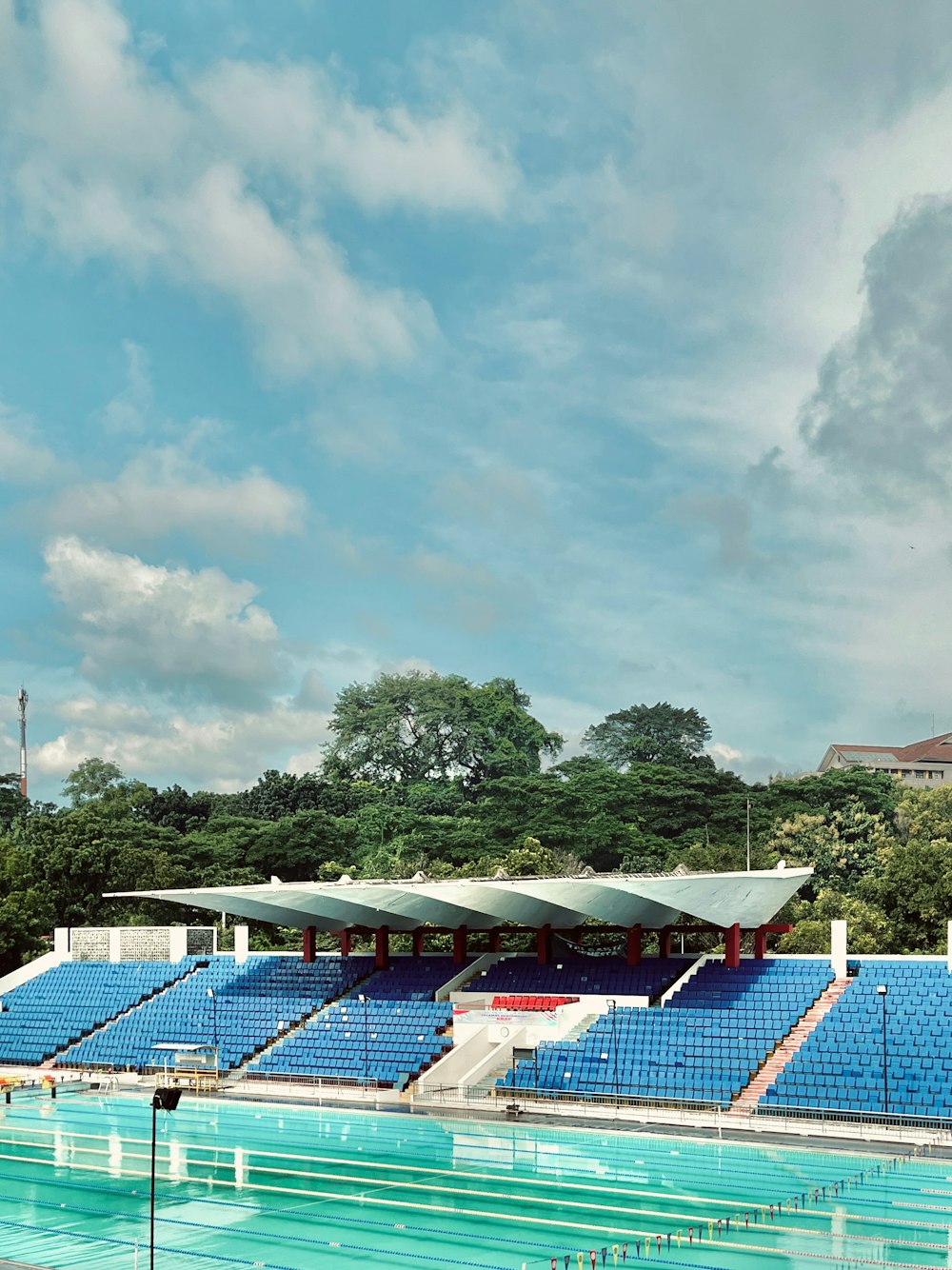 a large swimming pool with blue seats and trees in the background