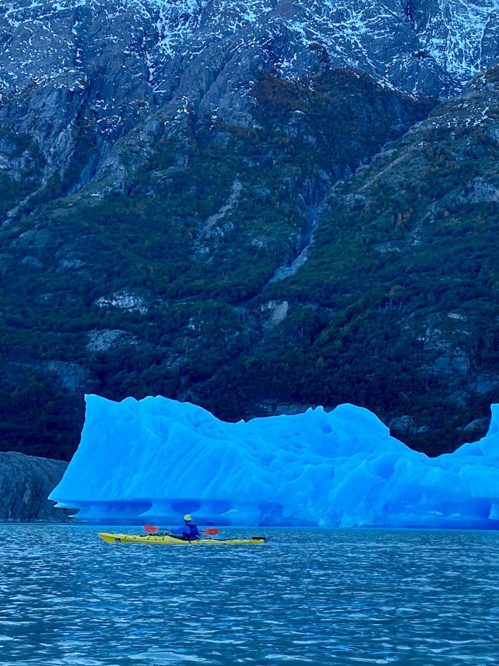 a person in a kayak in front of a large iceberg