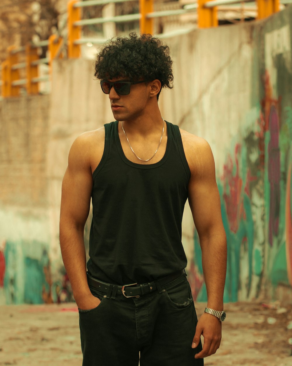 a man in a black tank top standing in front of a graffiti covered wall