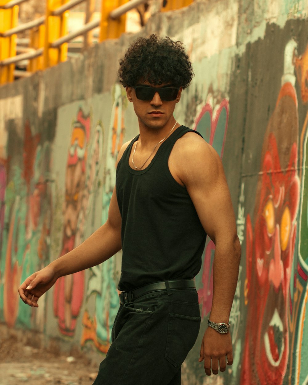 a young man wearing sunglasses standing in front of a graffiti covered wall