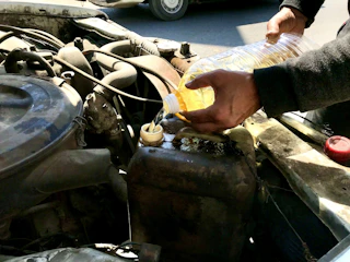 a man is filling a bottle of liquid into a car's engine