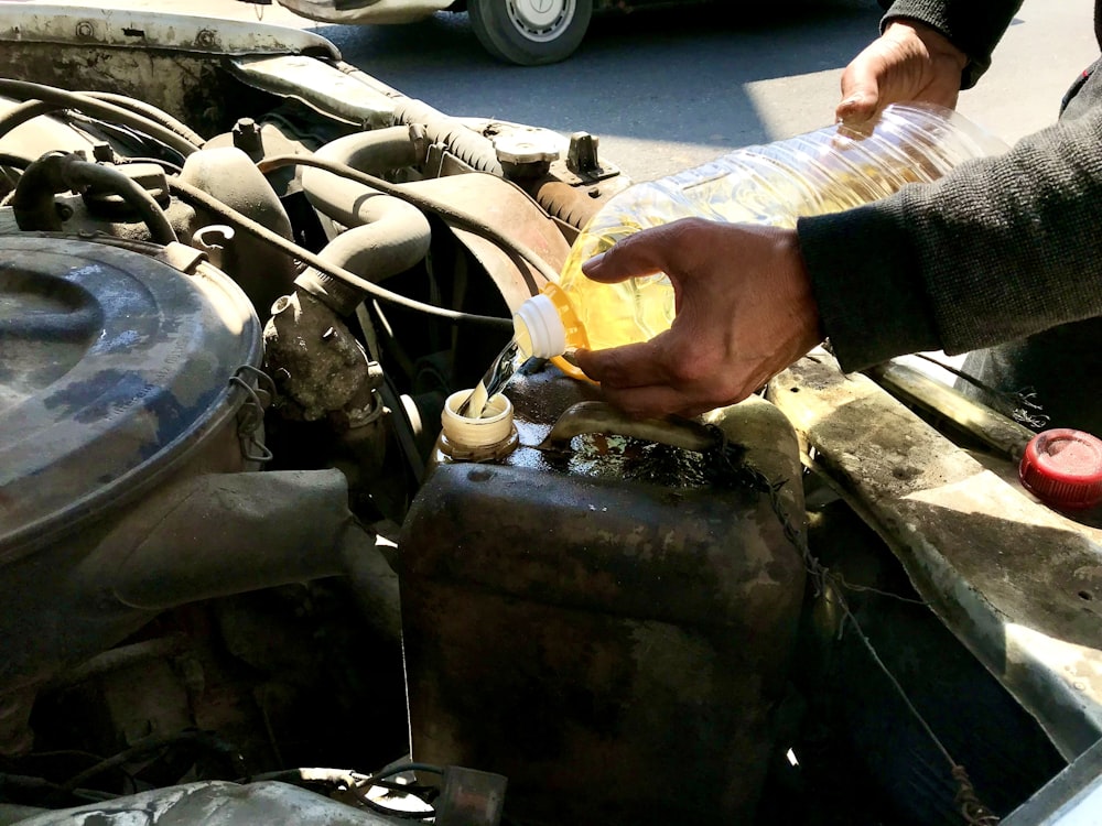 a man is filling a bottle of liquid into a car's engine