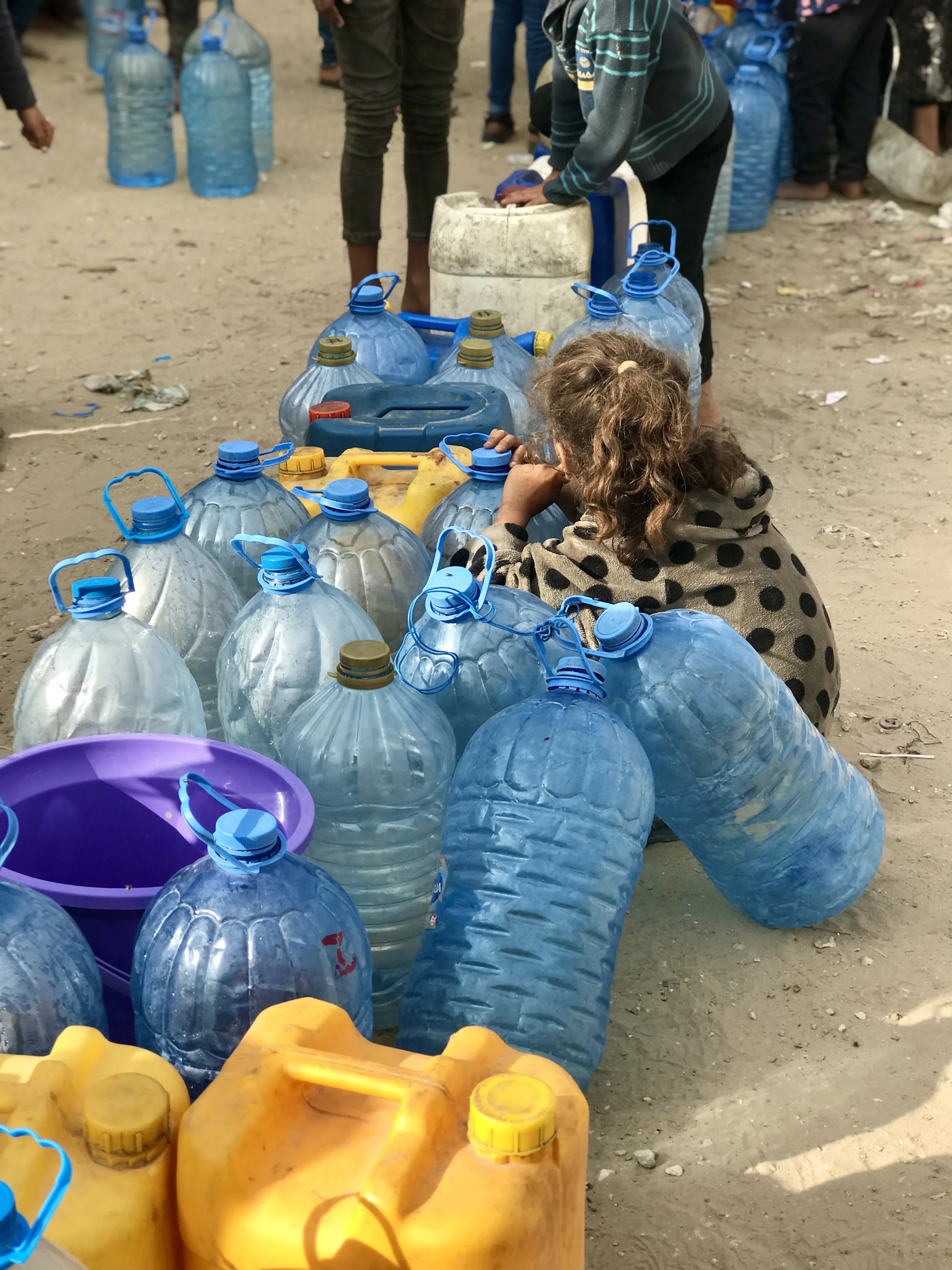 Ett barn sitter bland stora vattendunkar av plast vid en utdelningsplats