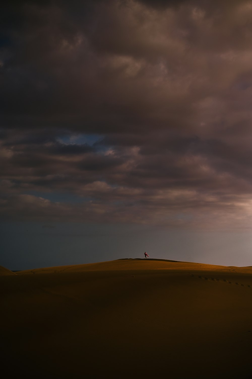 a lone person standing on top of a hill under a cloudy sky