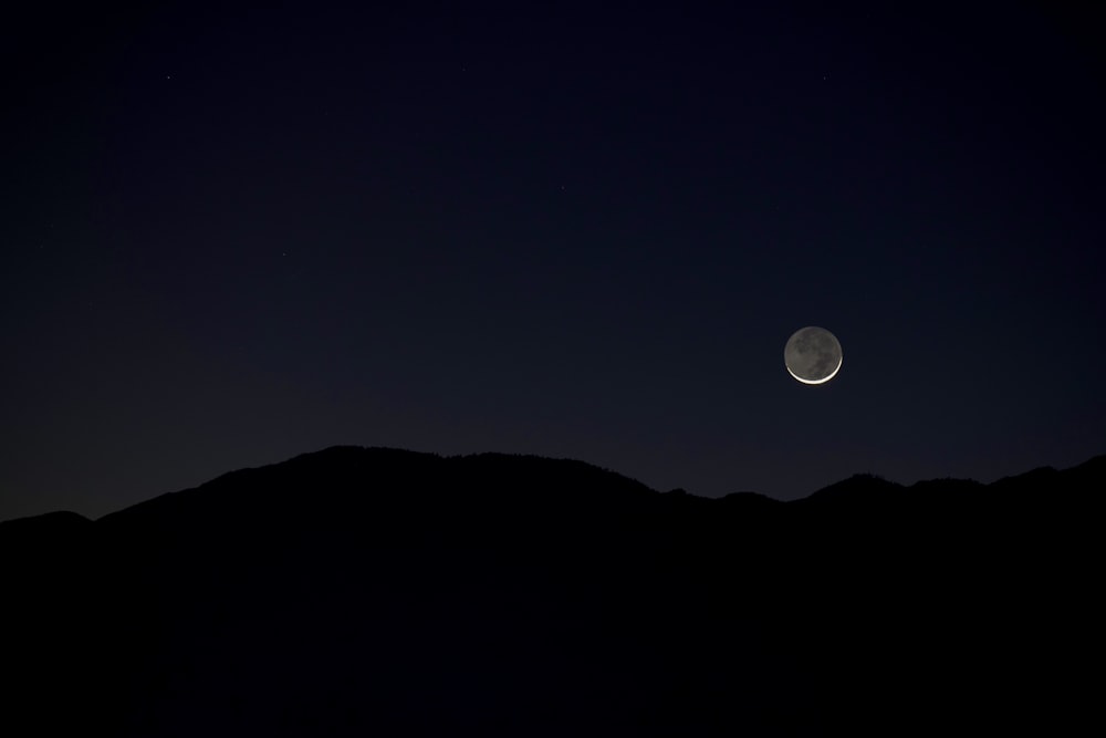 the moon is seen in the sky above a mountain