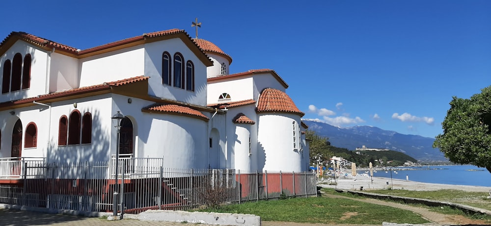 a white church with a red roof next to a body of water