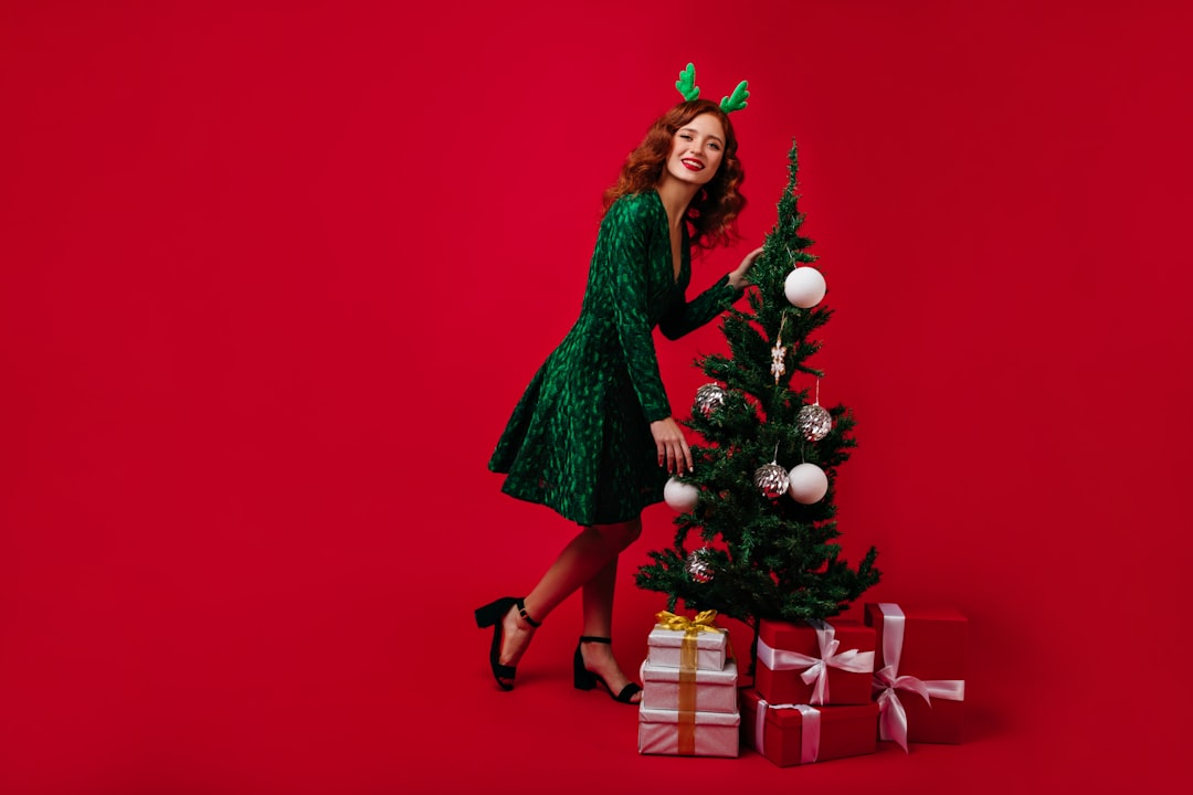 Happy girl in stylish green dress decorates Christmas tree. Full-length shot of lady with fiery curls.