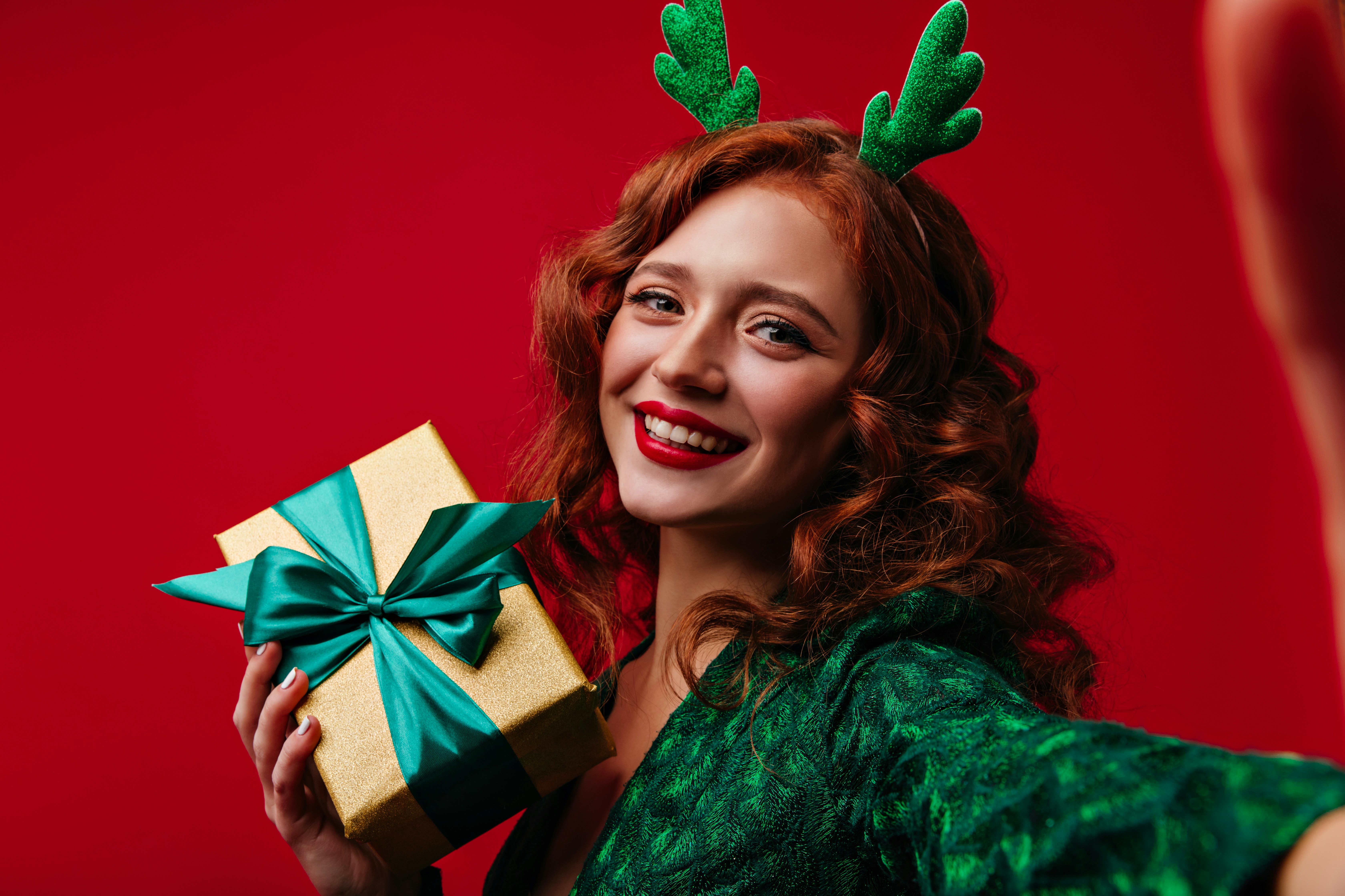 Joyful young woman with beautiful red lipstick on her lips takes selfie with Christmas box in her hands.