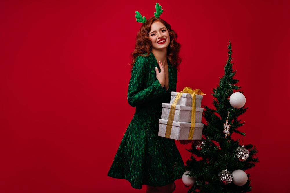 a woman in a green dress holding a present near a christmas tree