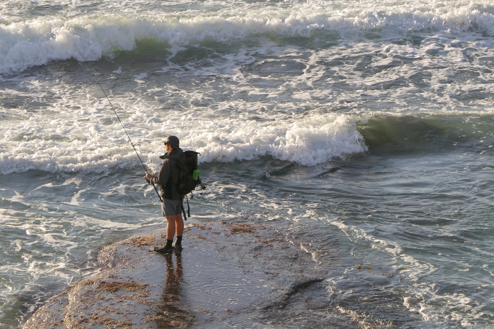 a man standing on top of a rock next to the ocean