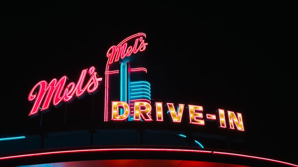 a neon sign above a drive - in at night
