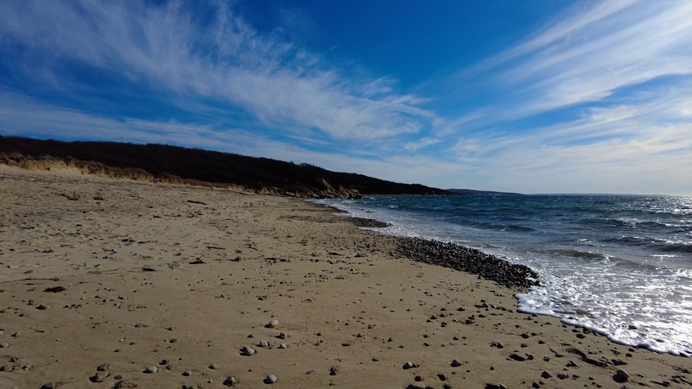 a sandy beach next to the ocean under a blue sky