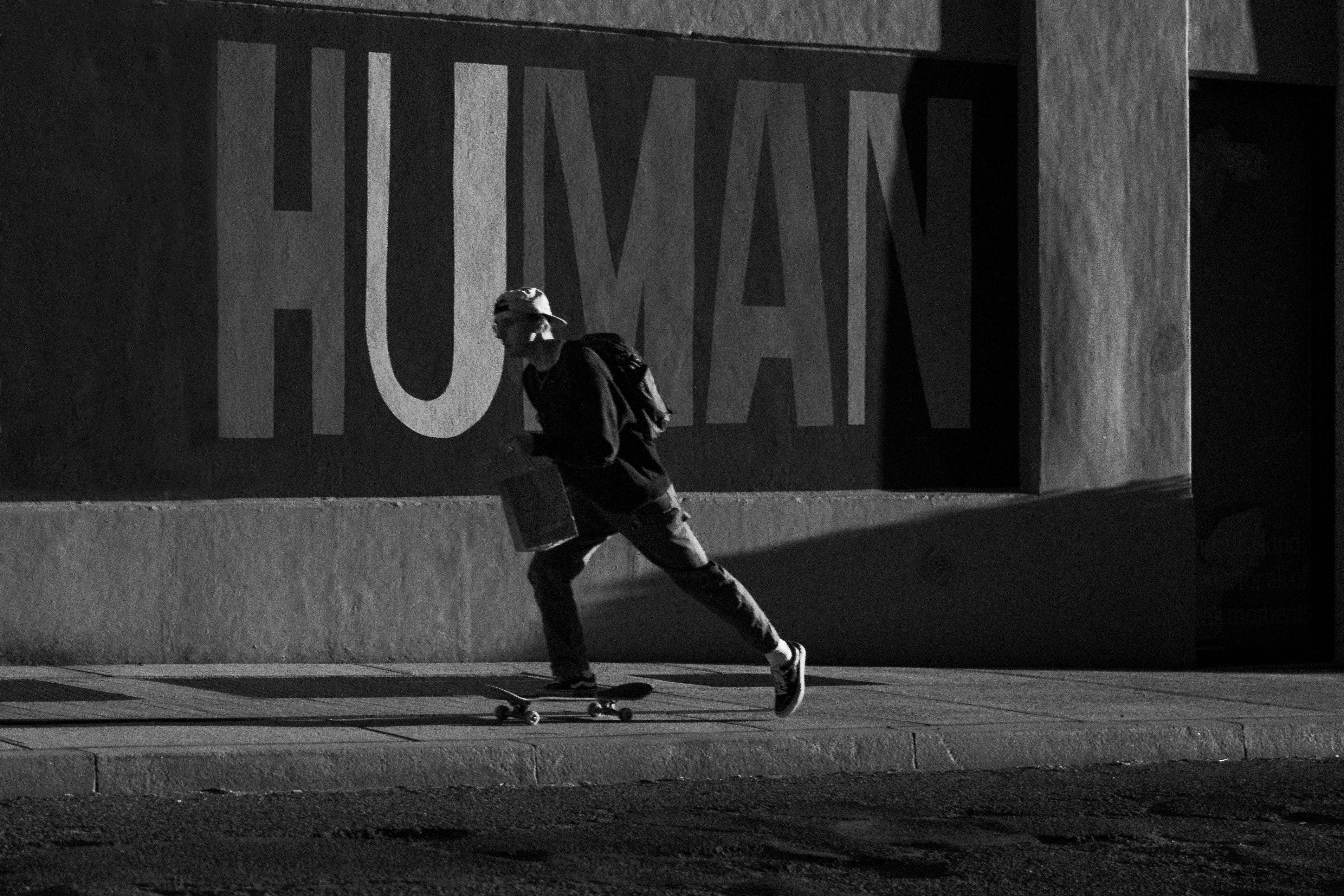 A man travels by skateboard on a sidewalk past a mural