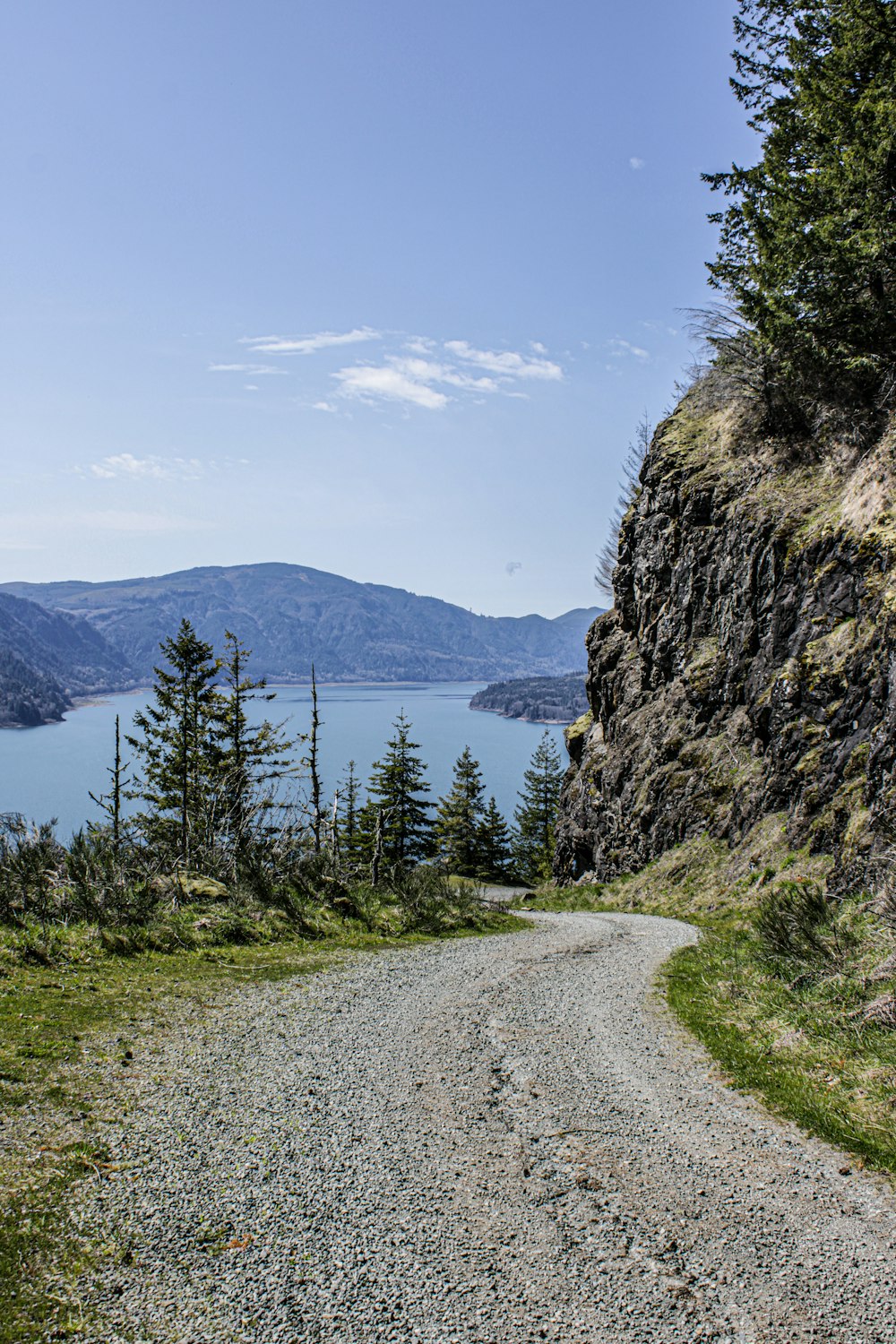 a gravel road going up a hill with a lake in the distance