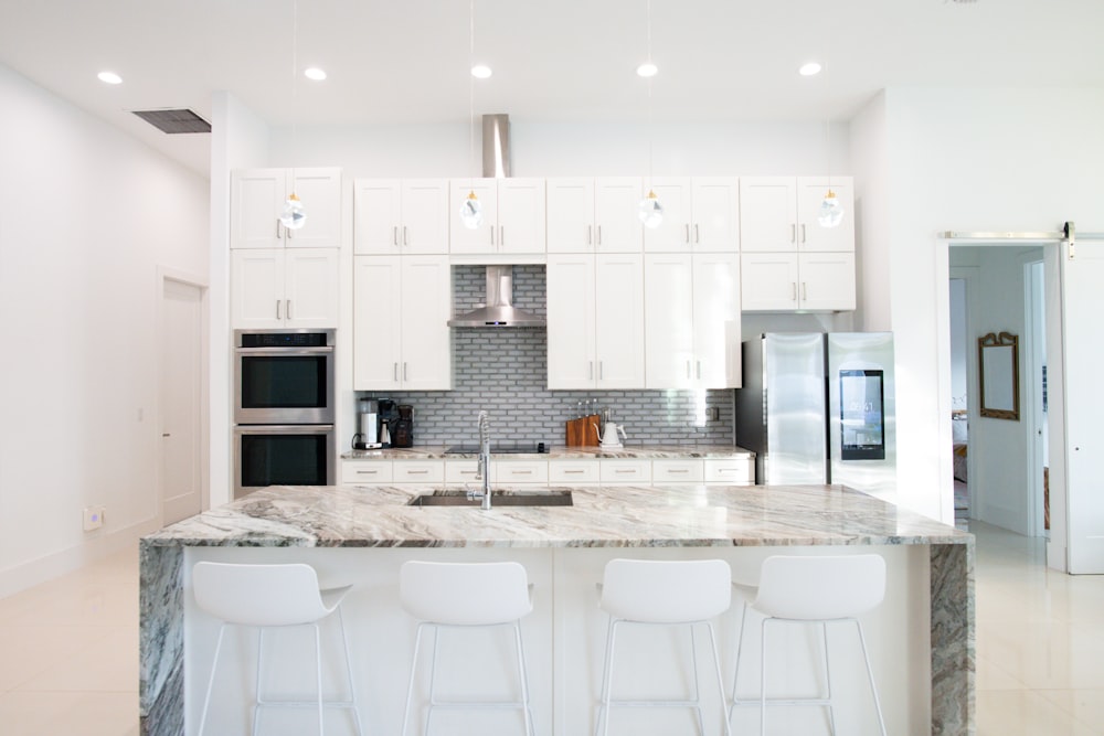 uma cozinha com armários brancos e bancadas de mármore