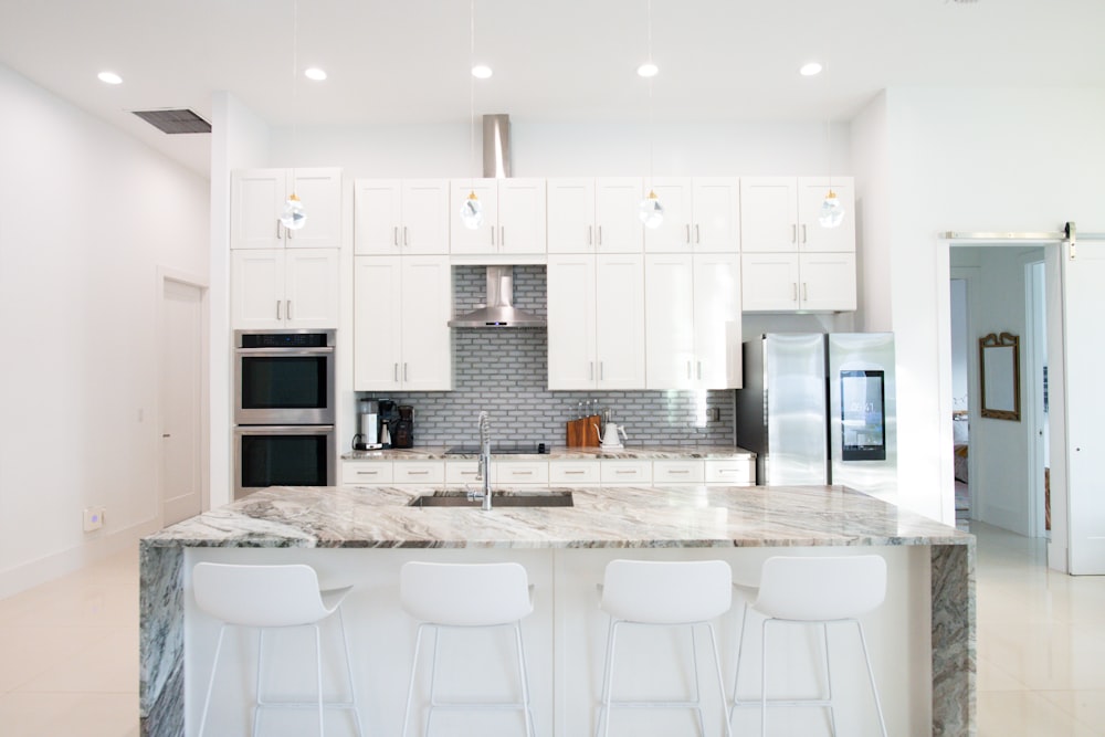 a kitchen with white cabinets and marble counter tops