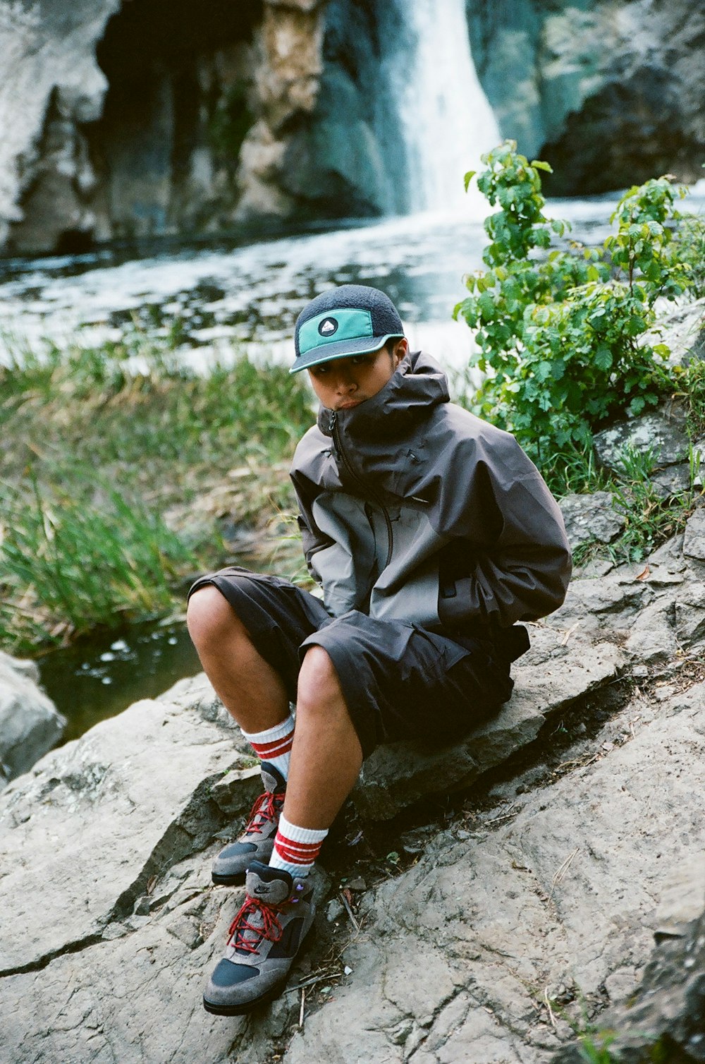 a boy sitting on a rock in front of a waterfall