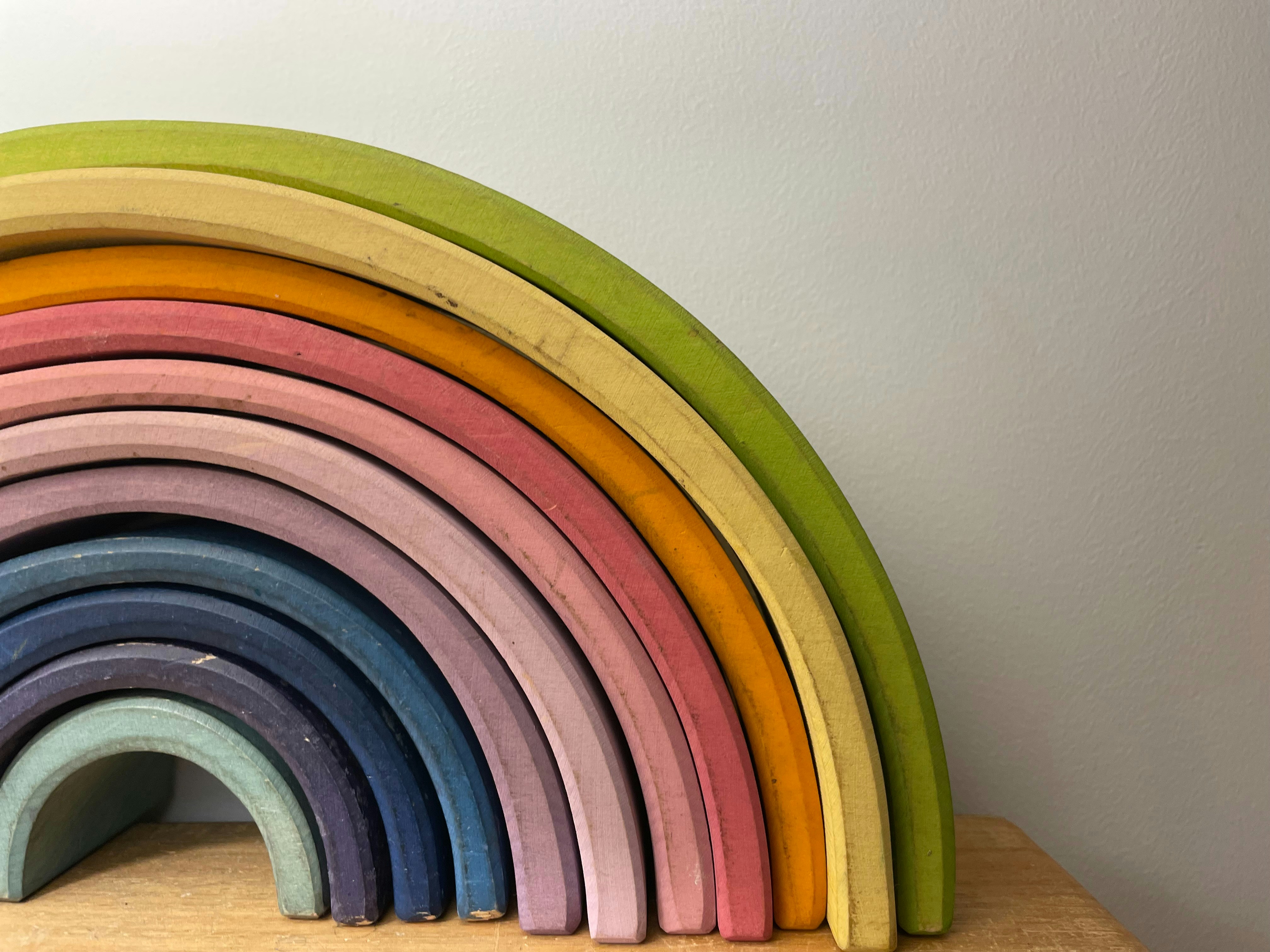 Colorful wooden rainbow stacker toy with arched pieces in red, orange, yellow, green and blue on a white surface
