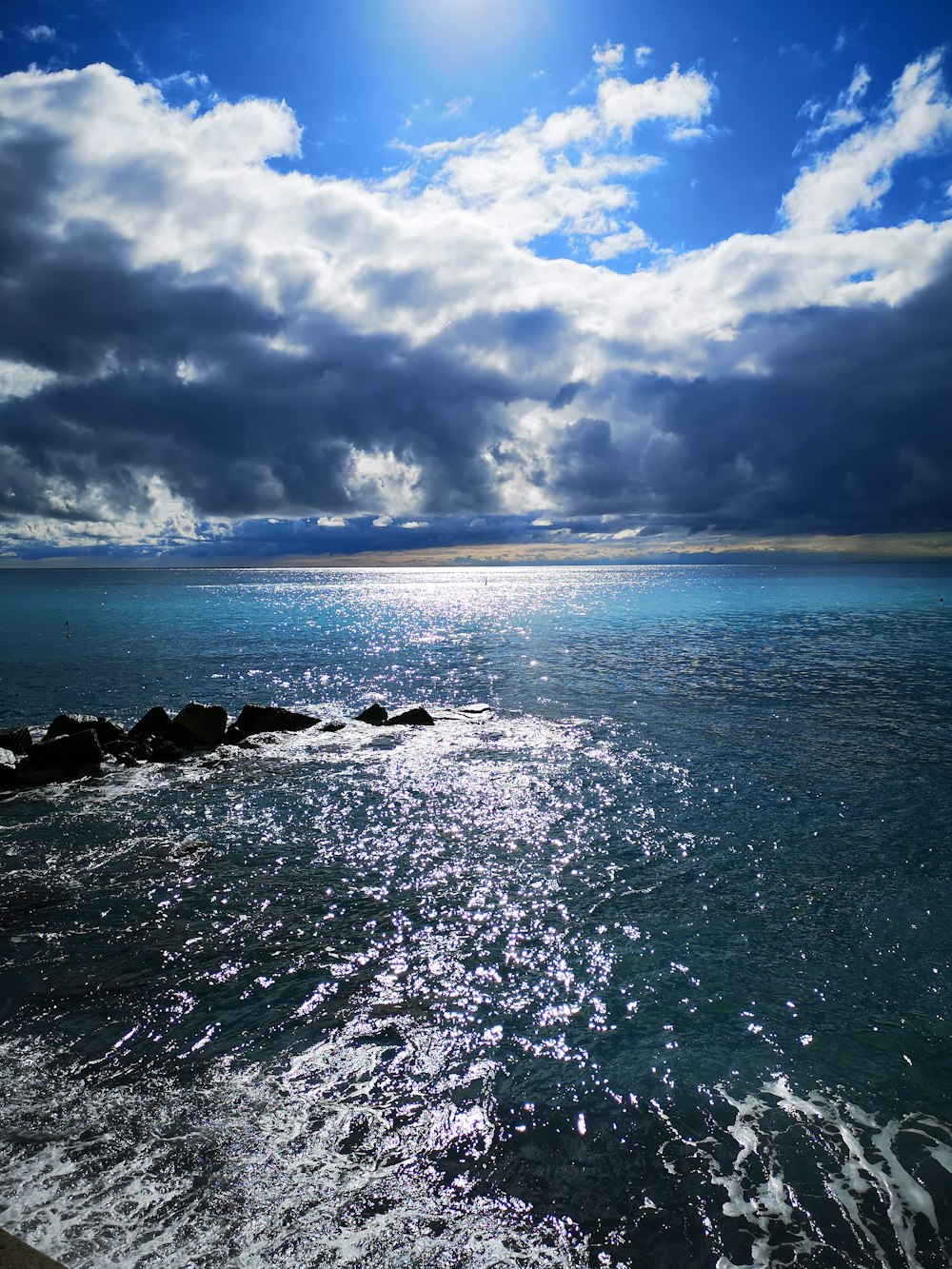 a body of water with rocks in the foreground and clouds in the background