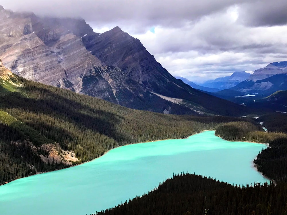 a lake surrounded by mountains and trees under a cloudy sky