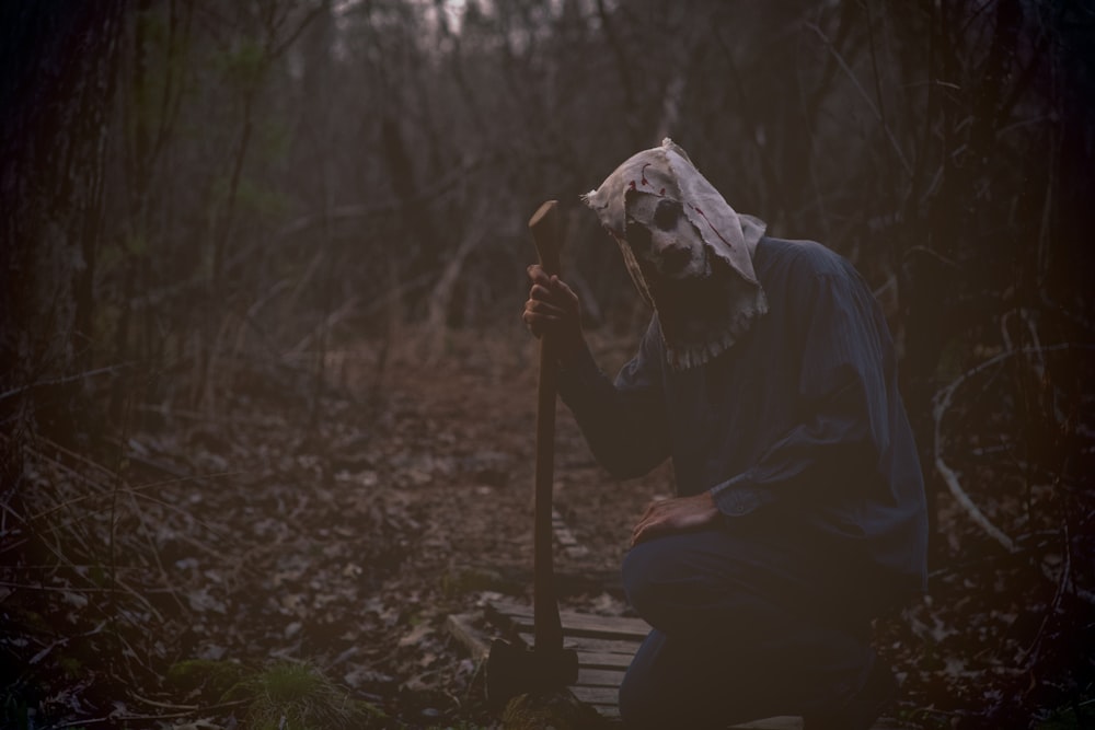 a person in a white mask crouching down in the woods
