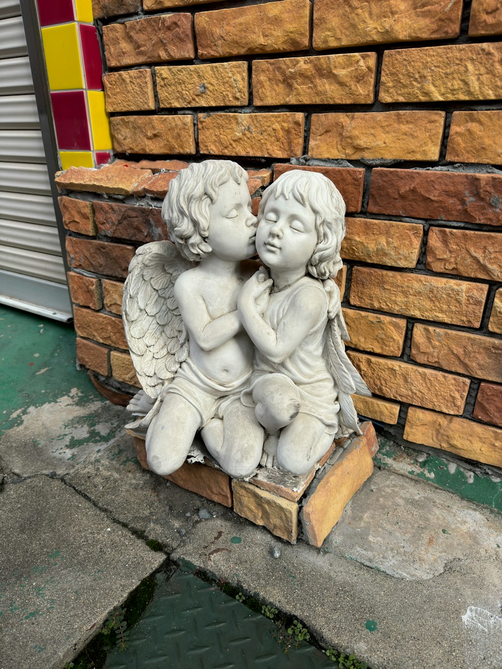 a statue of two cherubs sitting next to a brick wall