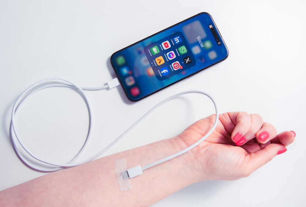 a woman's arm holding a cell phone and a charger attached to it