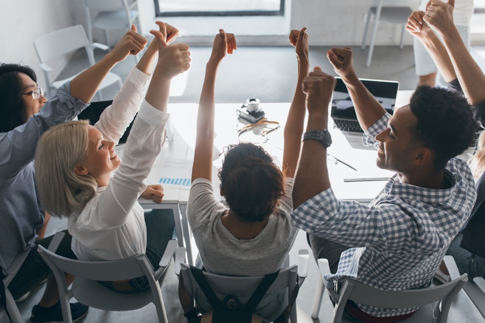 a group of people sitting at a table raising their hands