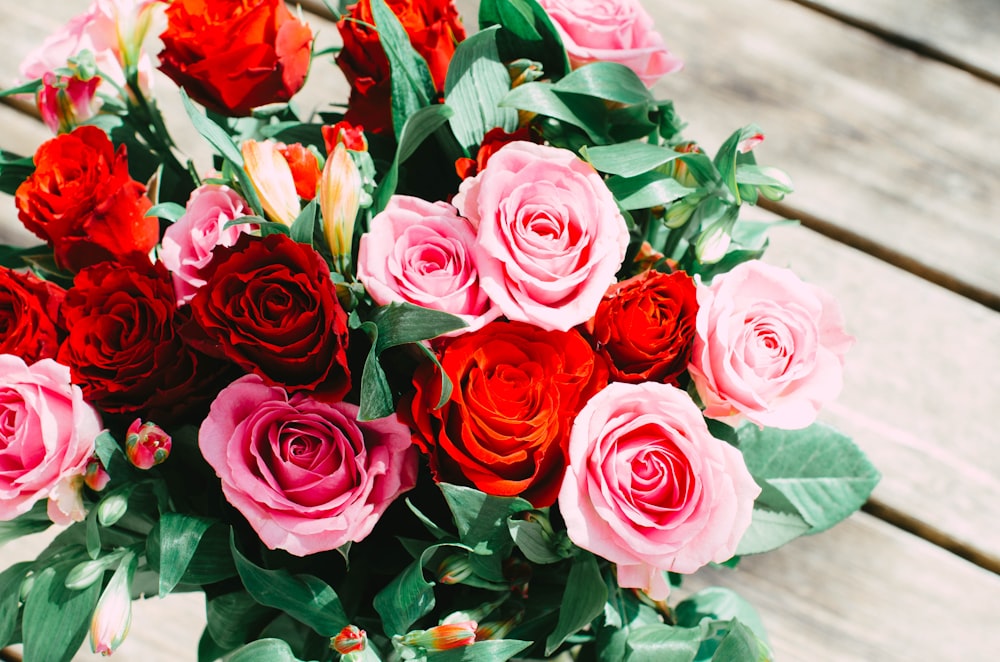 a bouquet of red and pink roses on a wooden table