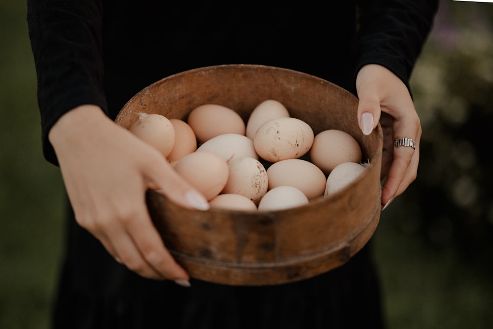 a woman holding a wooden bowl filled with eggs
