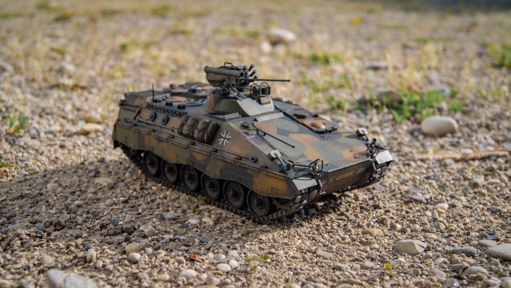 a toy tank sitting on top of a gravel field