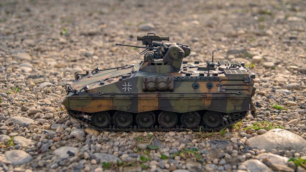 Un tanque de juguete del ejército sentado en la parte superior de un campo de grava