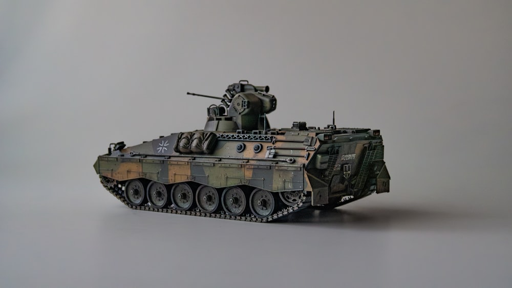um tanque militar camuflado é mostrado em um fundo cinza