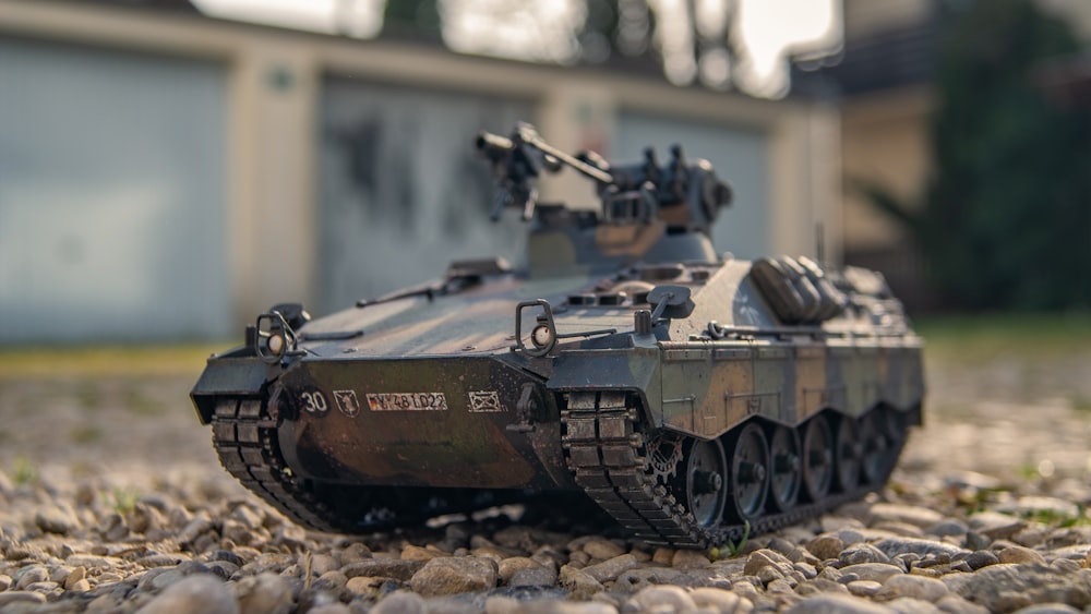 a toy tank sitting on top of a gravel covered ground