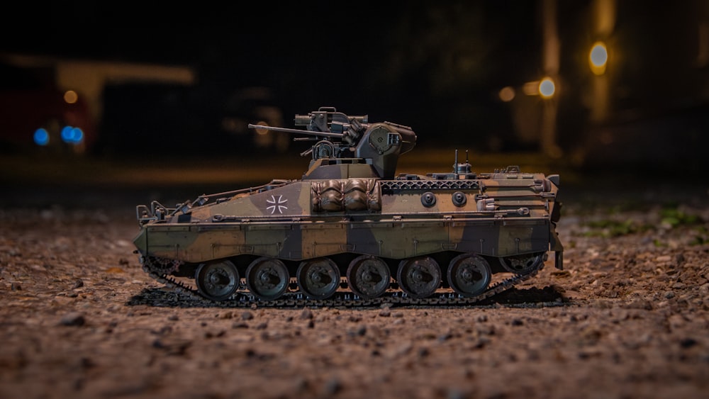 a toy army tank sitting on top of a dirt field