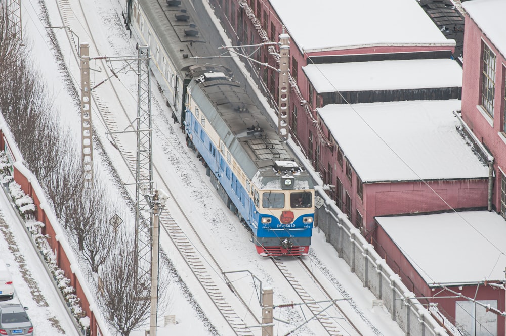 a blue train traveling down train tracks next to a red building