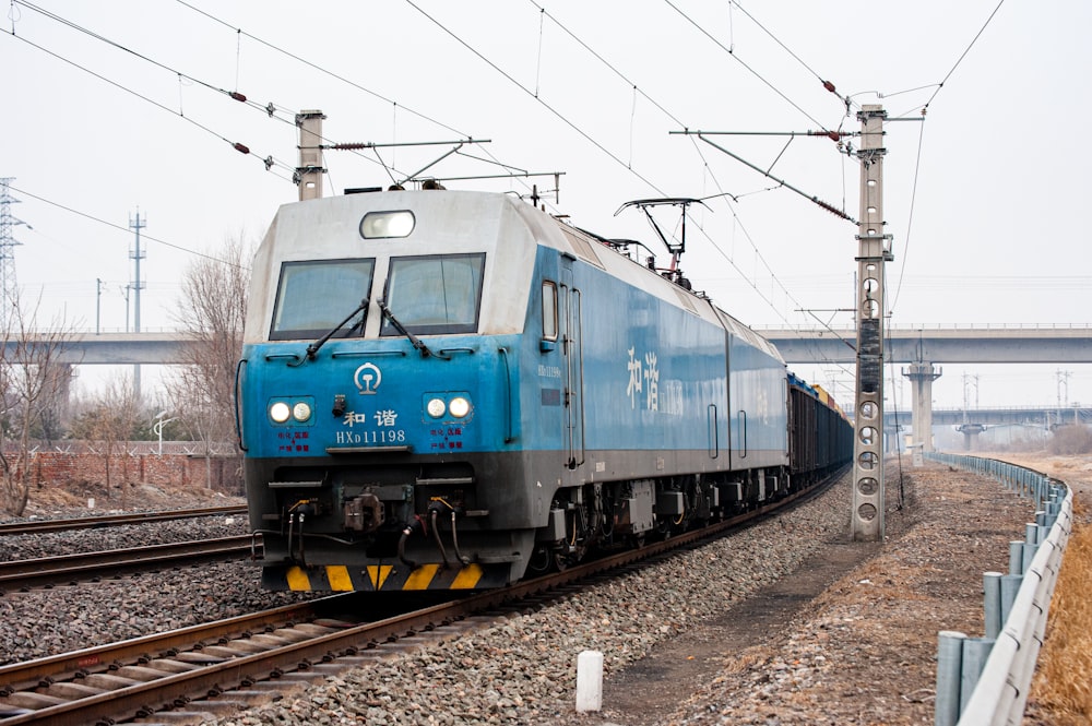 a blue train traveling down train tracks next to a bridge